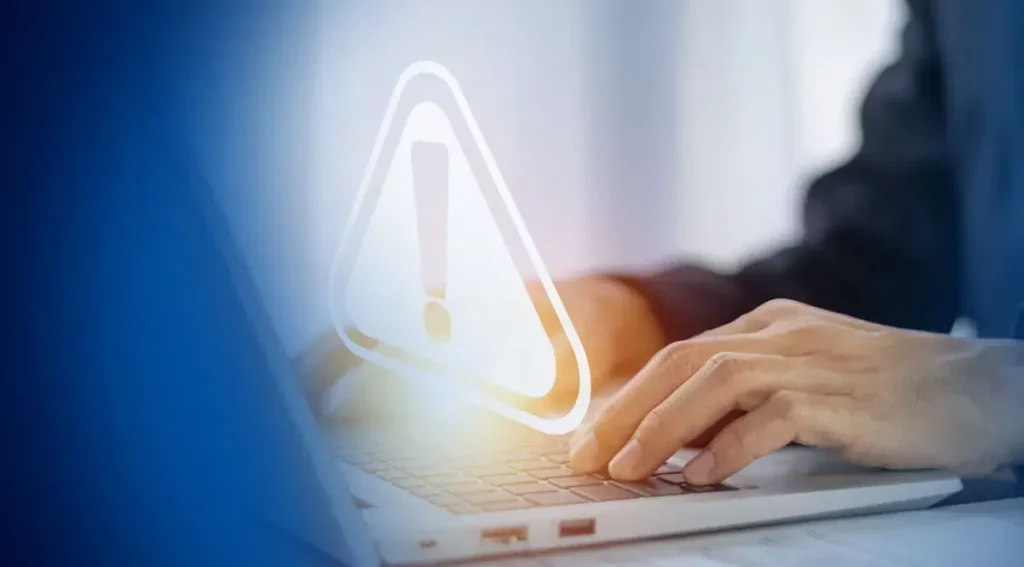 Person typing on a laptop with a warning symbol representing incident risk management